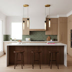 Three brass Clérachic pendant lights at staggered heights hang over a wood kitchen island with three dark wooden bar stools.