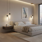 Two black and brass Clérachic pendant lights hang above a floating wood nightstand beside a bed with a beige headboard.