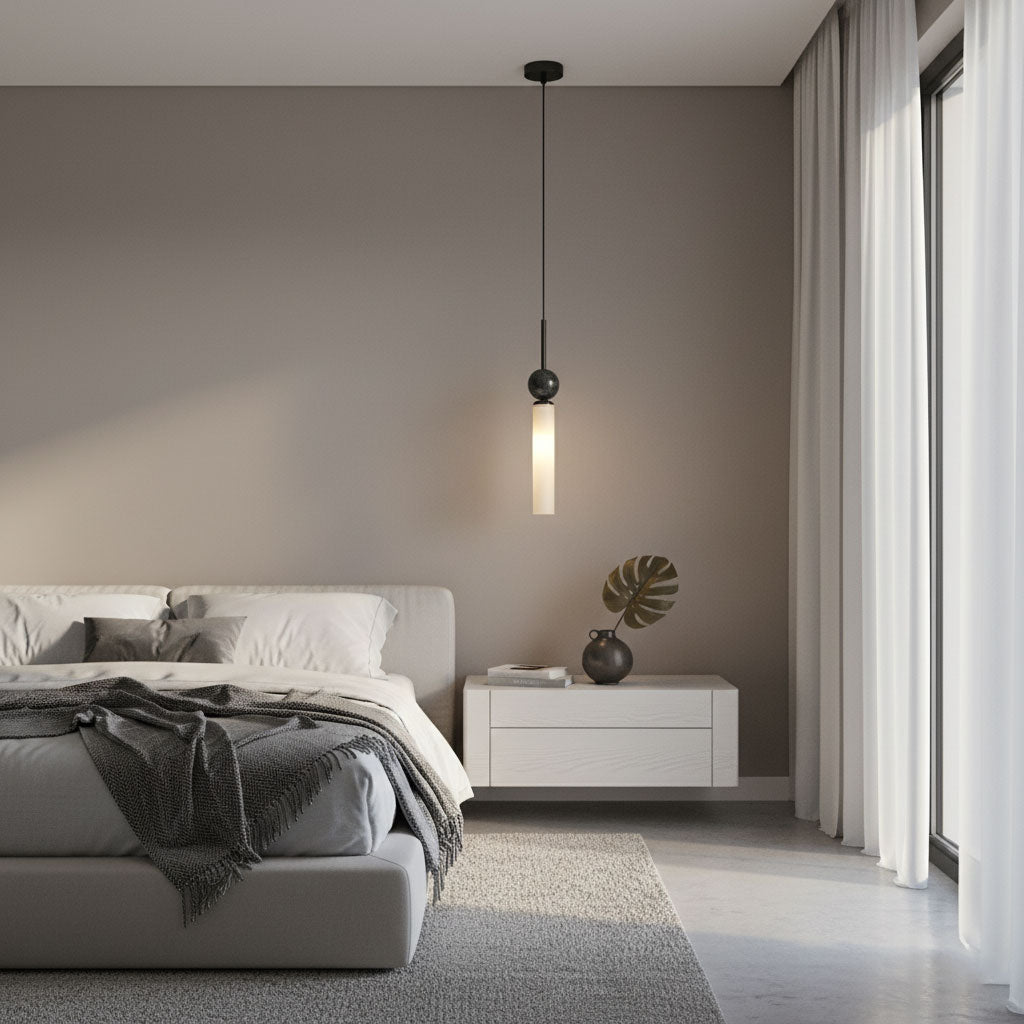 A single black marble Clérachic pendant light hangs beside a bed with a grey headboard, a white nightstand and a monstera sprig.