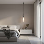 A single black marble Clérachic pendant light hangs beside a bed with a grey headboard, a white nightstand and a monstera sprig.