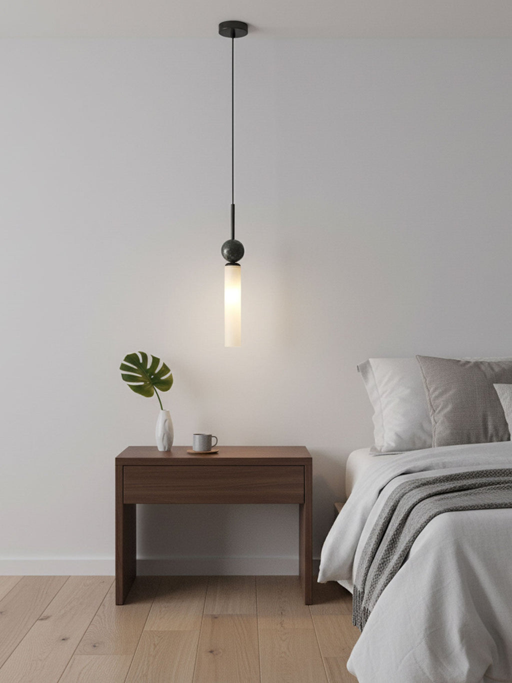 A single black Clérachic pendant light hangs above a wood nightstand holding a small vase and cup beside a bed with white linen.