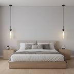 Two black marble Clérachic pendant lights hang symmetrically above a bed with a beige headboard and matching nightstands.