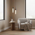 Two black Clérachic pendant lights hang in a corner nook, lighting a round side table and an armchair with a folded throw.