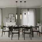 Three black Clérachic pendant lights hang above a dark dining table with black chairs, set against a sage-green wall and fireplace.