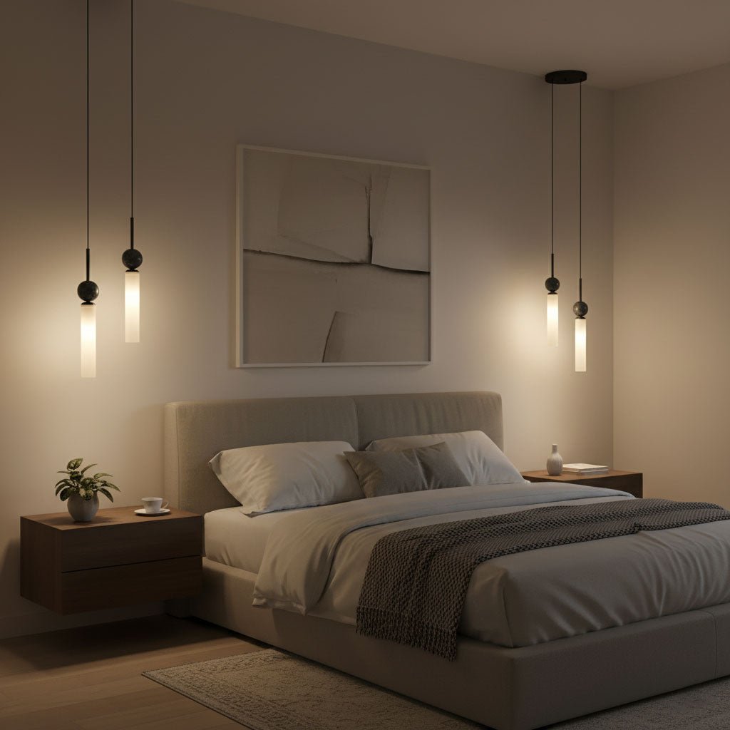 Three black Clérachic pendant lights at staggered heights glow above a bed with a tufted grey headboard and framed wall art.