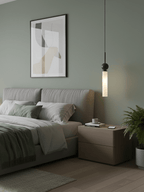 A single black marble Clérachic pendant light hangs beside a bed with a grey-blue headboard on a sage wall, above a nightstand.