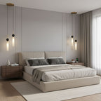 Two black and two brass Clérachic pendant lights hang together above a bed with a beige headboard, comparing both finishes.