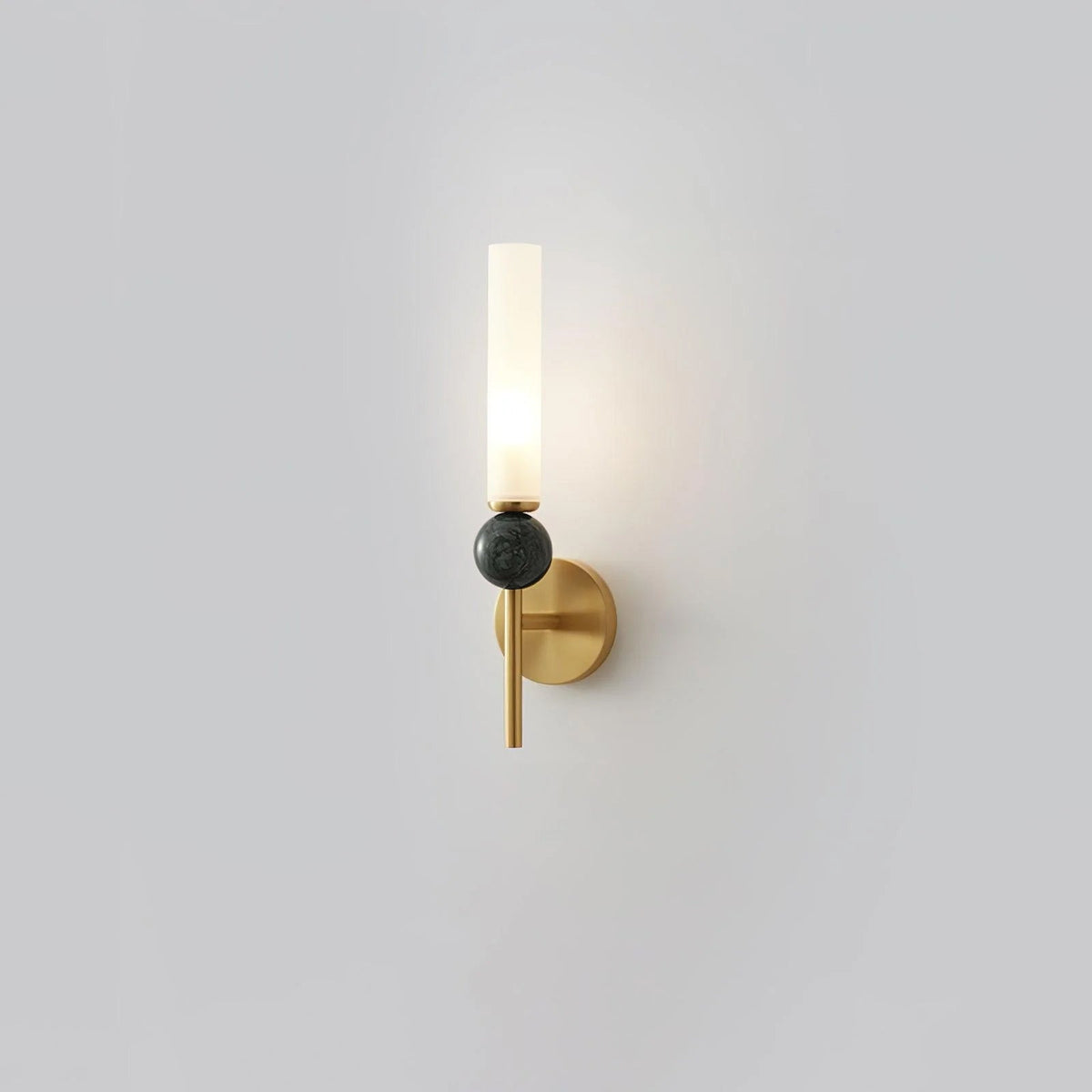 Set alone against grey, this Clérachic brass-arm wall sconce holds a green marble orb, lit at the top.