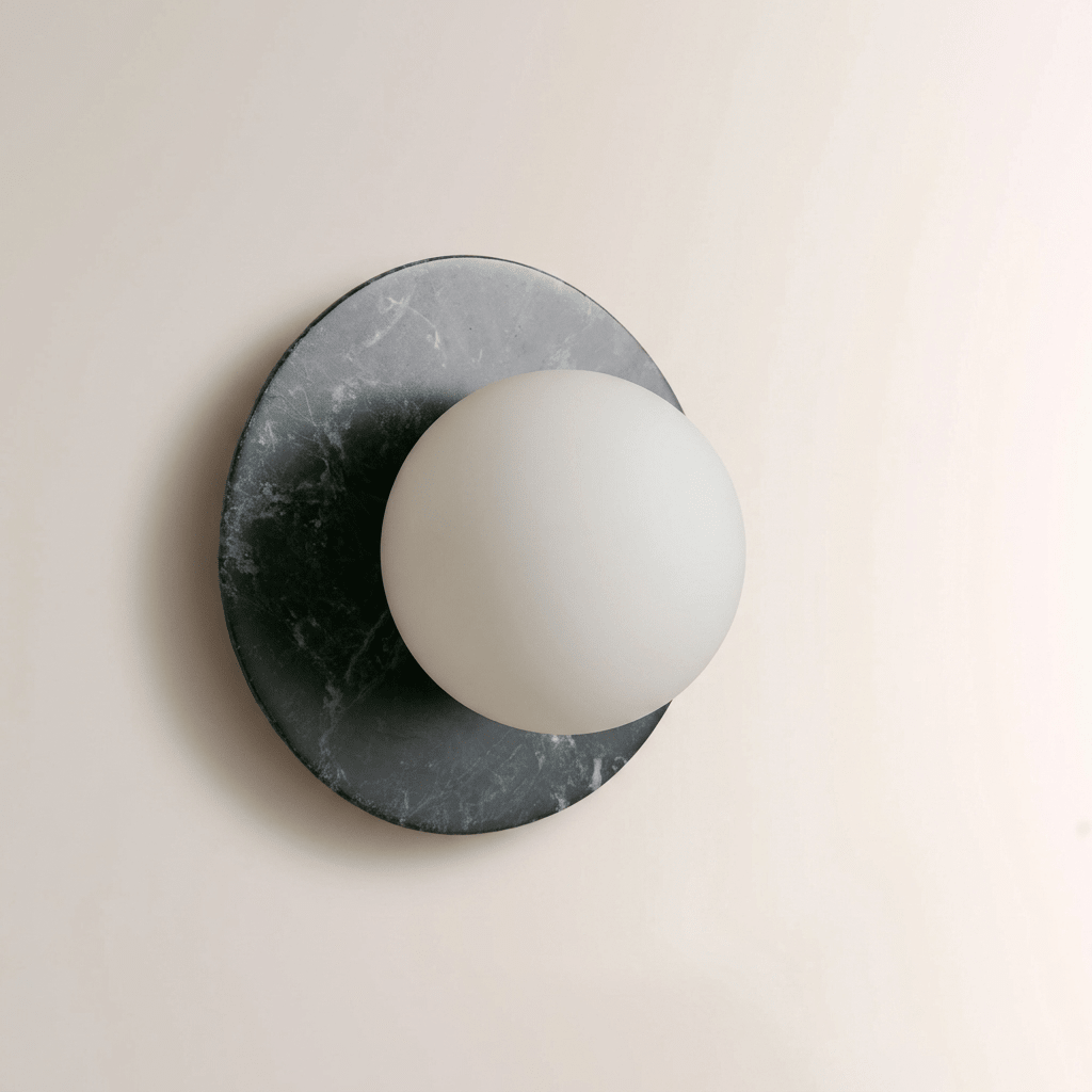 Close-up of a Clérachic wall sconce in dark green-grey marble, the frosted white globe unlit against the stone's pale veining.