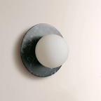 Close-up of a Clérachic wall sconce in dark green-grey marble, the frosted white globe unlit against the stone's pale veining.
