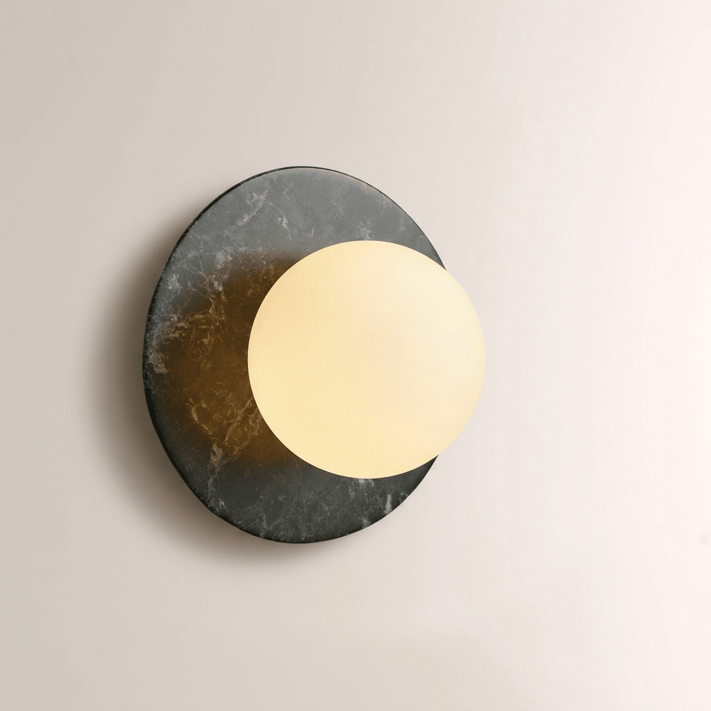 Close-up of a Clérachic wall sconce in dark marble, its opal globe glowing warm gold against the stone's mottled surface.
