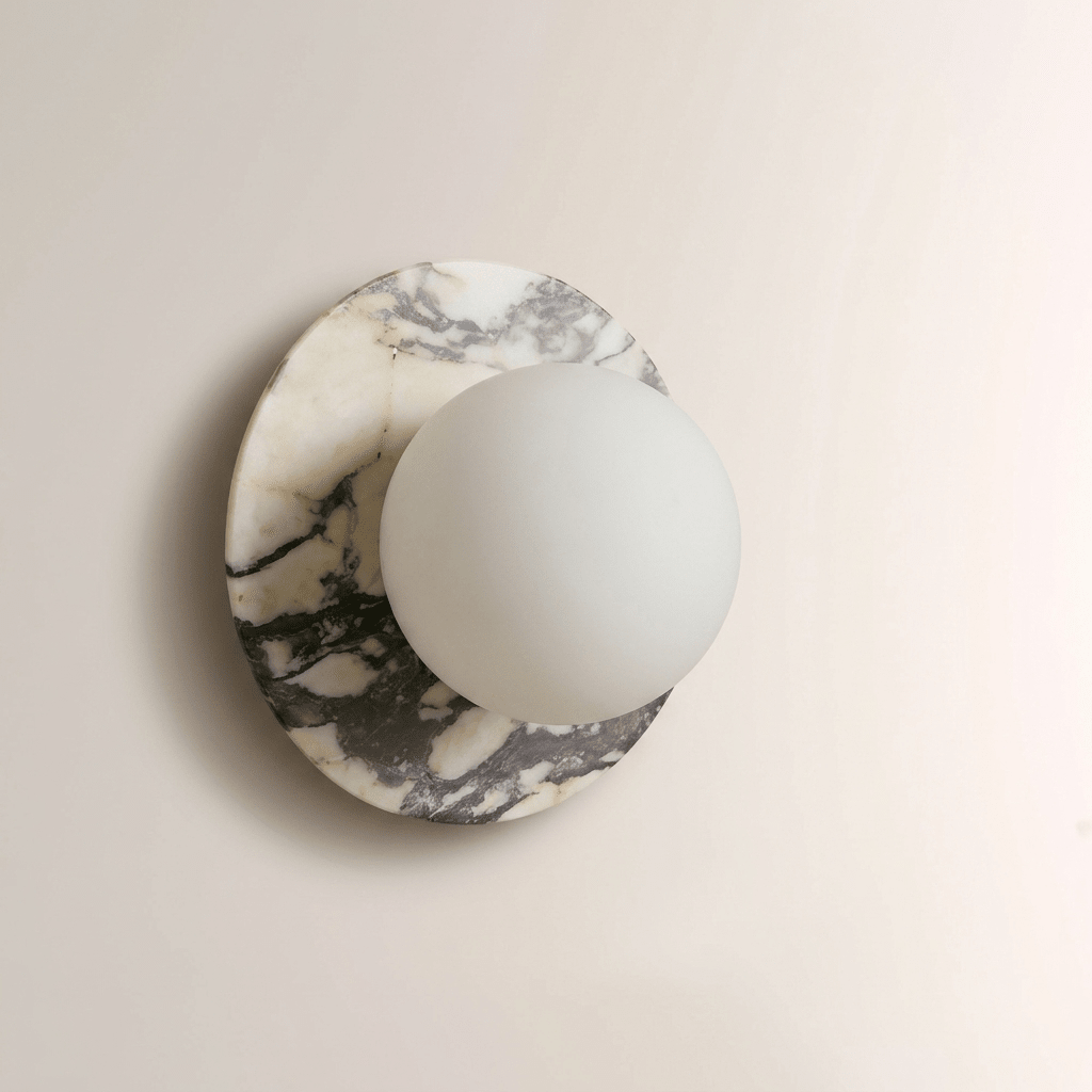 Grey-veined white marble surrounds this Clérachic wall sconce, the frosted glass globe unlit against the natural stone pattern.