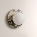 A second close-up of the grey-veined marble Clérachic wall sconce, showing the opal globe seated flush against the disc's edge.