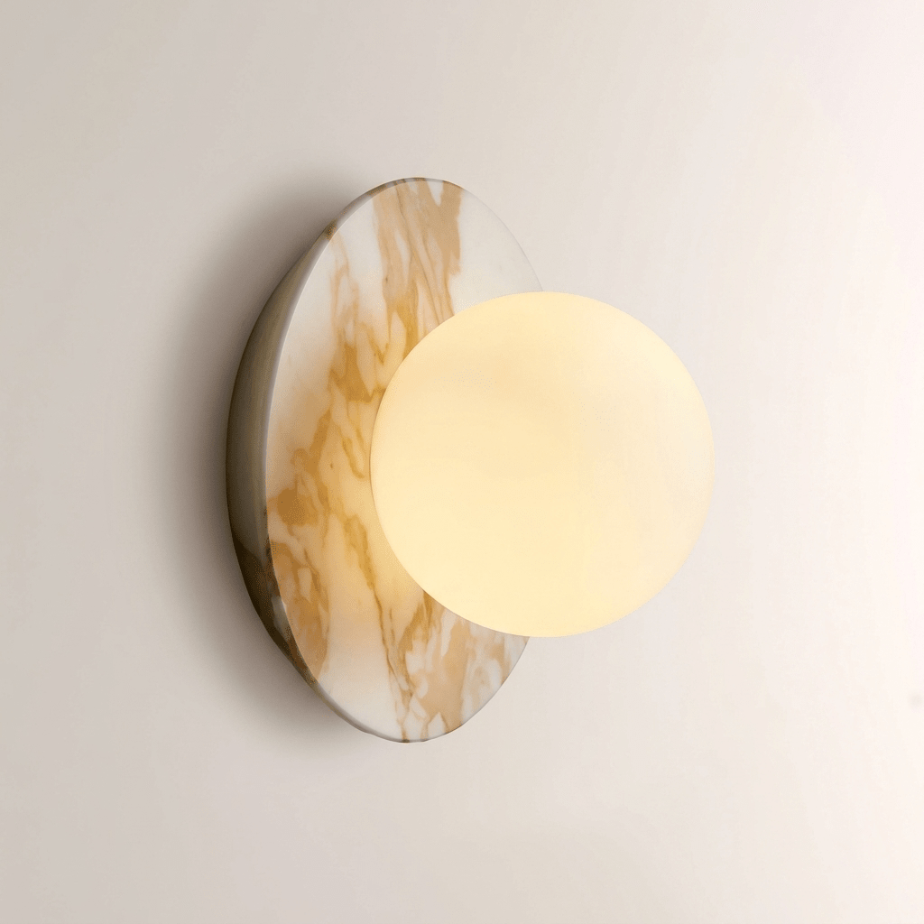 Close-up of a Clérachic wall sconce in gold-veined white marble, its opal glass globe glowing warm against the stone.