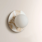 Gold-veined white marble frames this Clérachic wall sconce, the frosted globe unlit and pale against the warm stone tones.