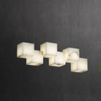 Six-head Ivnoros chandelier lit against a dark charcoal wall, each alabaster cube glowing warm.
