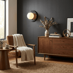 Clérachic's marble disc sconce lights a charcoal-painted wall above a walnut credenza, next to a tan armchair with a wool throw.