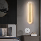 Clérachic selvia wall light lit beside a bed and nightstand, the brass bar bright against pale grey plaster