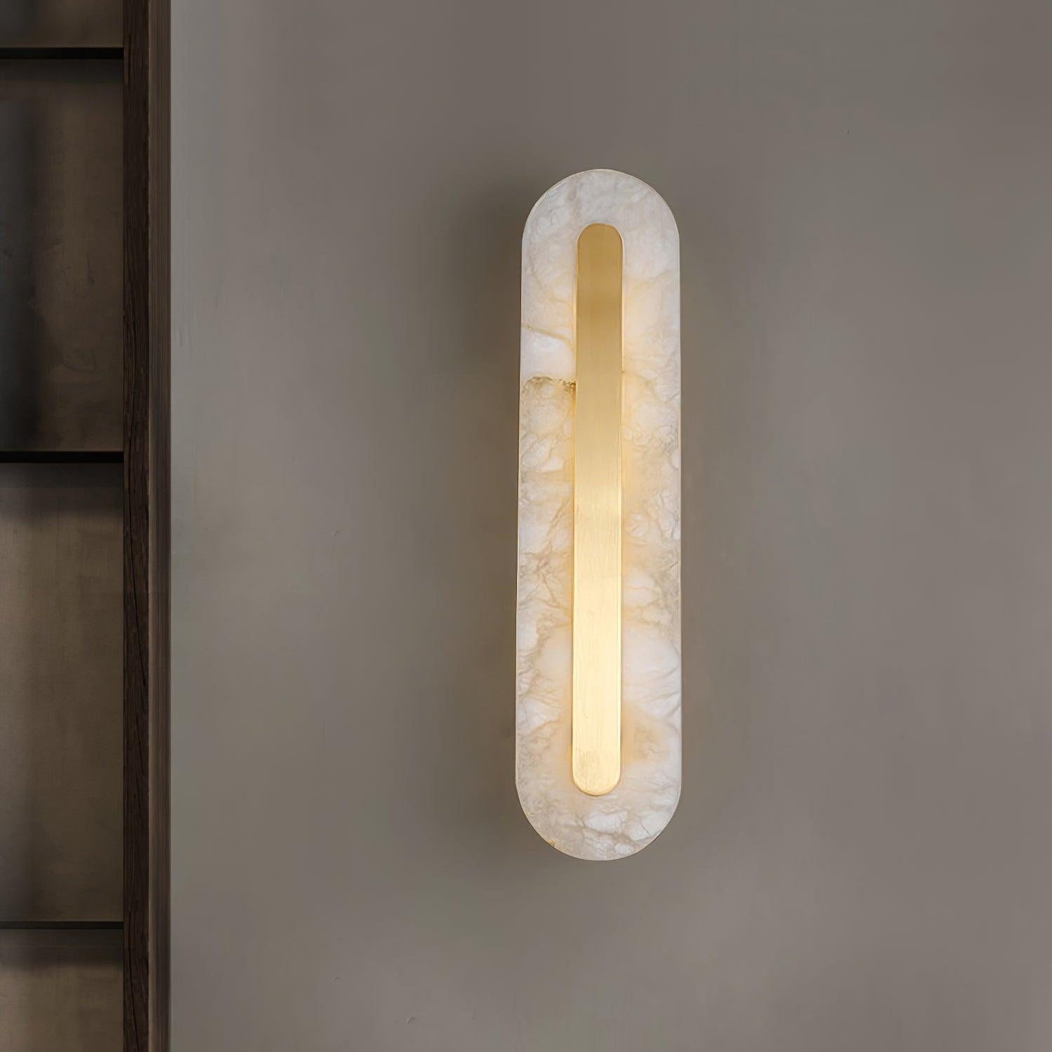 Clérachic selvia wall light lit and centred on a warm grey wall next to a dark shelving unit
