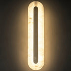 Clérachic selvia wall light in a darkened room, the alabaster shade fully backlit around the brass bar