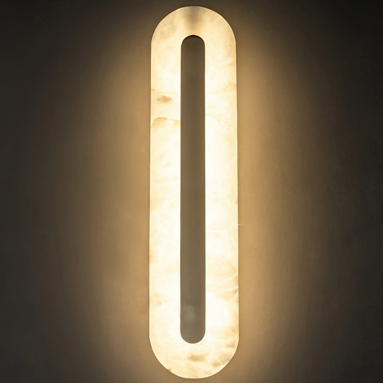 Clérachic selvia wall light in a darkened room, the alabaster shade fully backlit around the brass bar