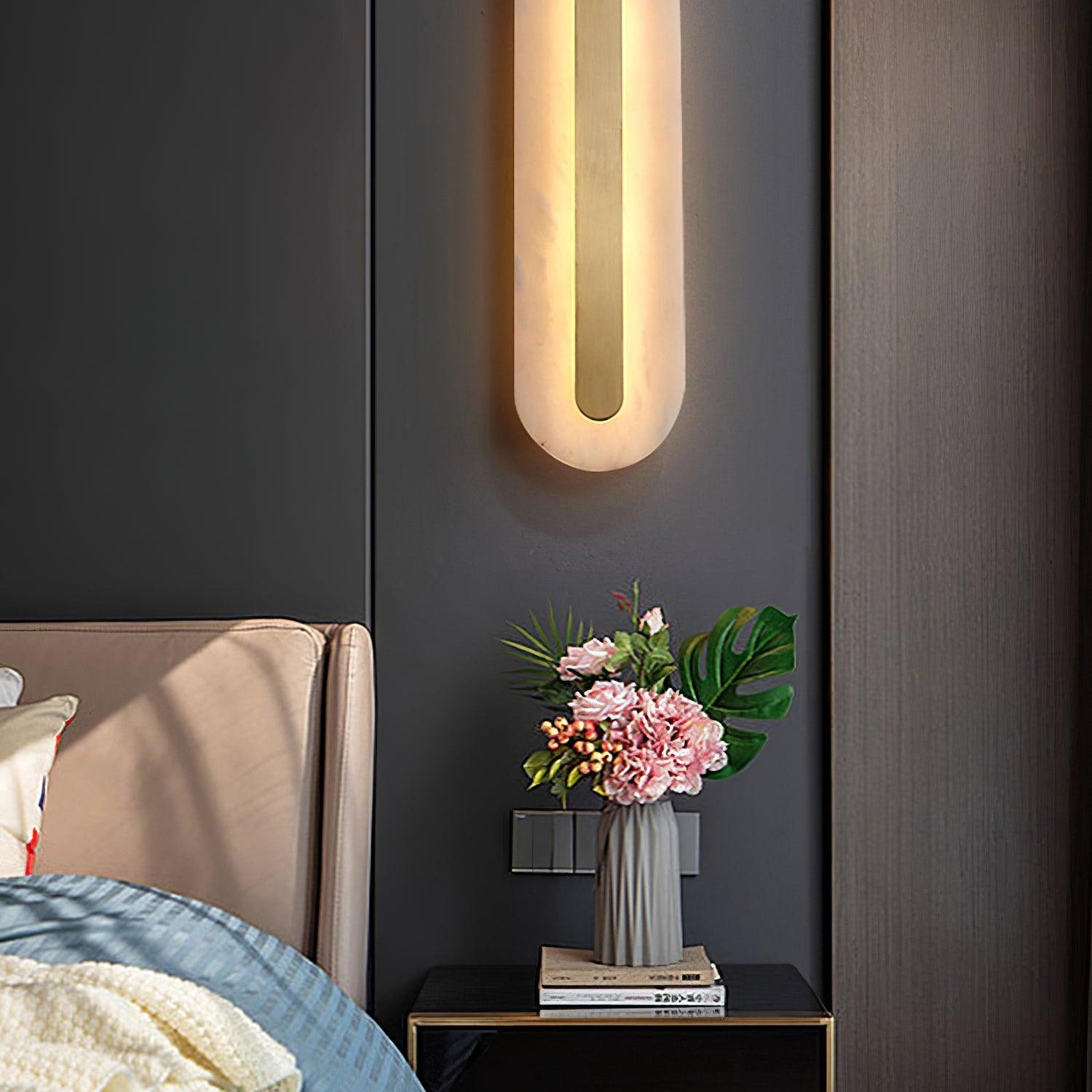 Clérachic close crop of the Selvia wall light lit above a bedside table on a dark charcoal panelled wall
