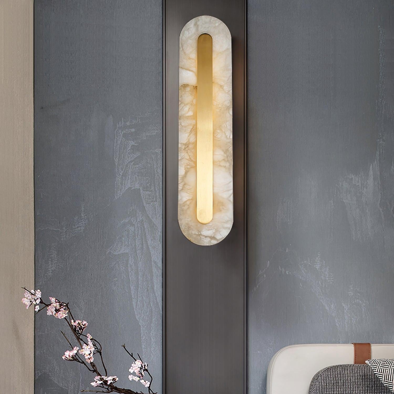 Clérachic selvia wall light glowing on a bronze-trimmed panel in a grey hallway, cherry blossom branch below