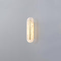 The Clérachic compact Selvia wall light on a grey wall, alabaster shade backlit and casting a soft shadow