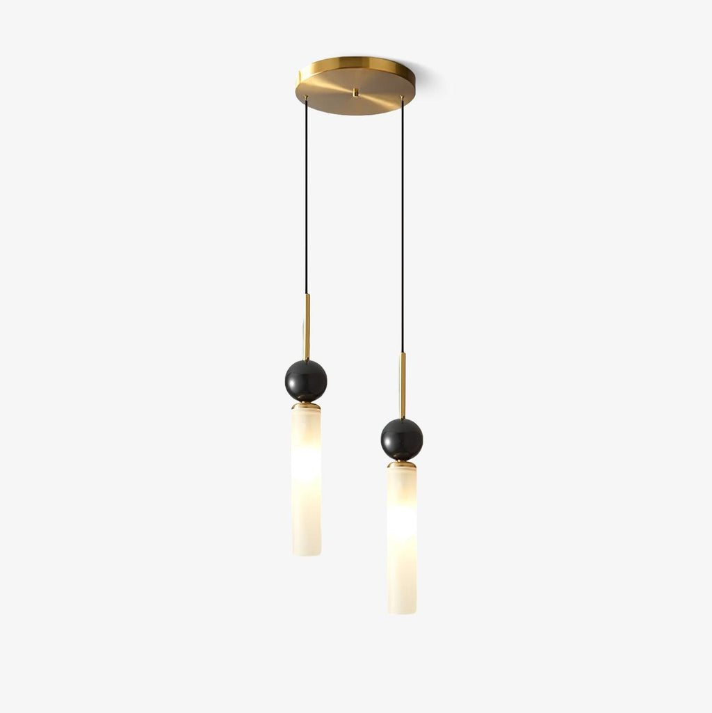 Two Clérachic pendants at staggered lengths hang from one round brass canopy, each glass cylinder topped with a dark marble sphere.