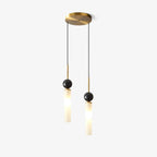 Two Clérachic pendants at staggered lengths hang from one round brass canopy, each glass cylinder topped with a dark marble sphere.