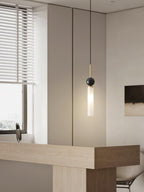 A close-up of a single black marble Clérachic pendant light beside a window with blinds and a light wood countertop.