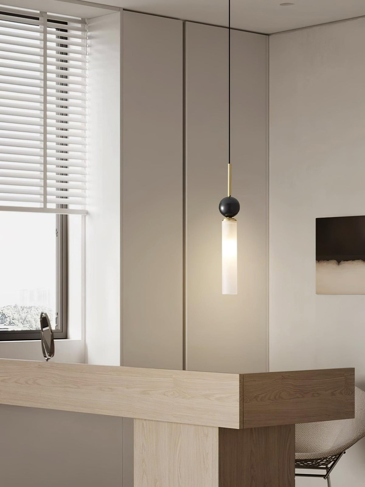A close-up of a single black marble Clérachic pendant light beside a window with blinds and a light wood countertop.