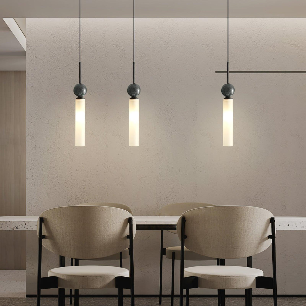 Three black Clérachic pendant lights at staggered heights hang above a plaster-walled dining nook with beige chairs.