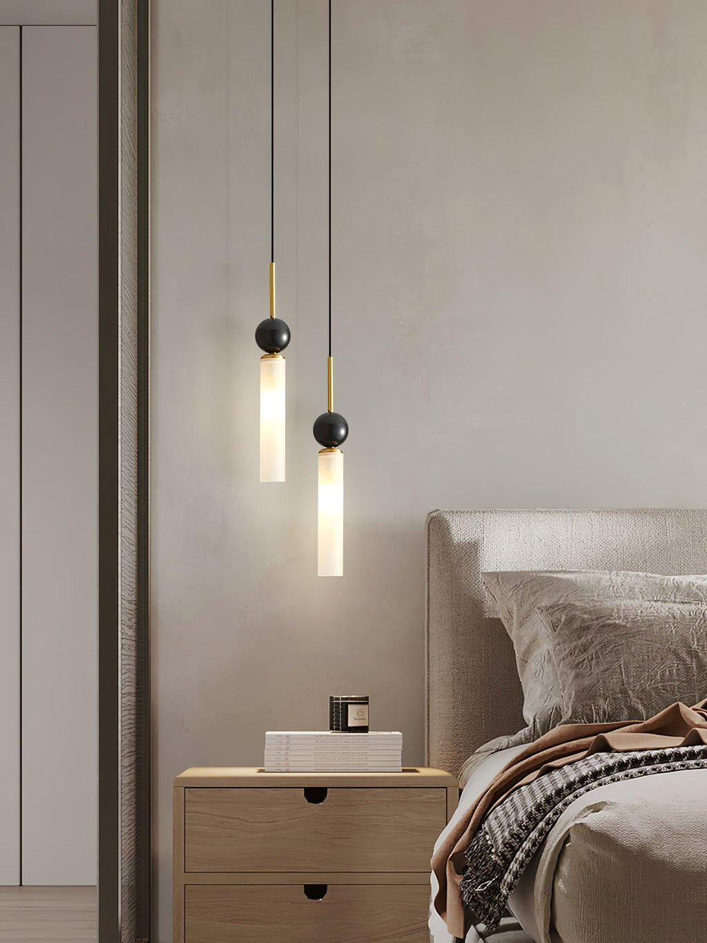 A close-up of two black Clérachic pendant lights beside an upholstered bed and a wood nightstand holding a small candle.