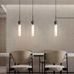 Three black marble Clérachic pendant lights hang above a dining table, casting warm light over two beige upholstered chairs.