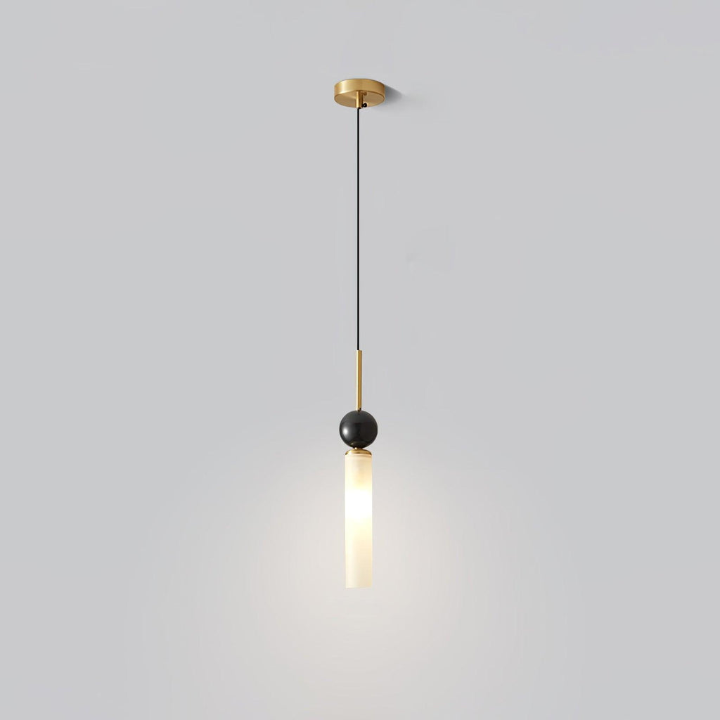 A studio shot of a single-head Clérachic pendant light with a brass canopy and stem, its marble ball and frosted shade lit.