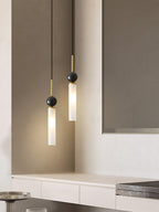A close-up of two staggered black Clérachic pendant lights above a pale stone counter, with a mirror reflecting the room behind.