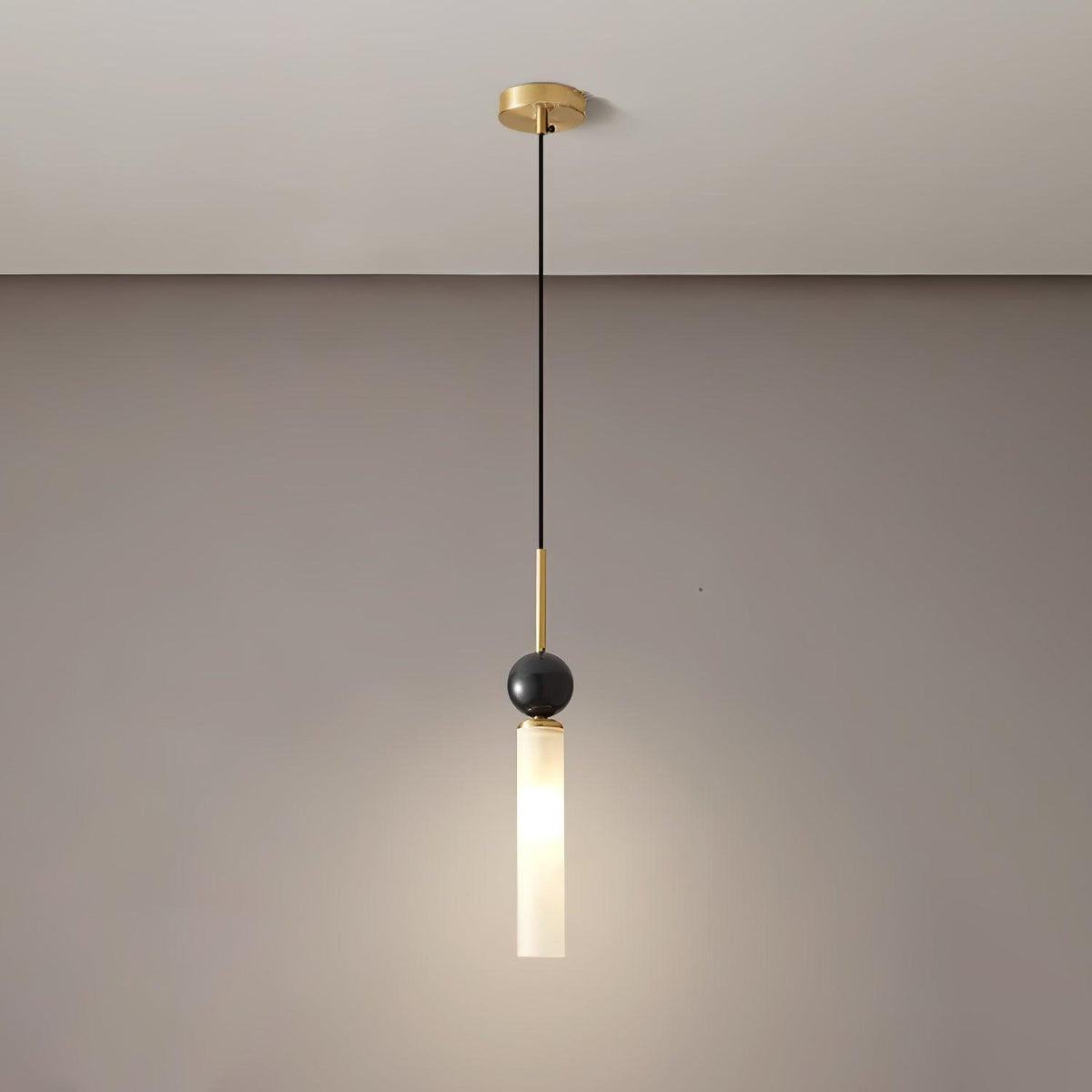 A studio shot of a single Clérachic pendant light on a white background, showing the black marble ball and cylinder shade up close.