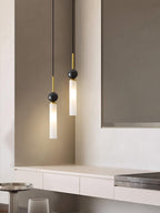 A close-up of two staggered black Clérachic pendant lights near a mirror above a pale wood countertop and a bar stool.