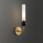 A Clérachic brass wall sconce with a black marble orb glows against a dark charcoal wall in a moodily lit room.