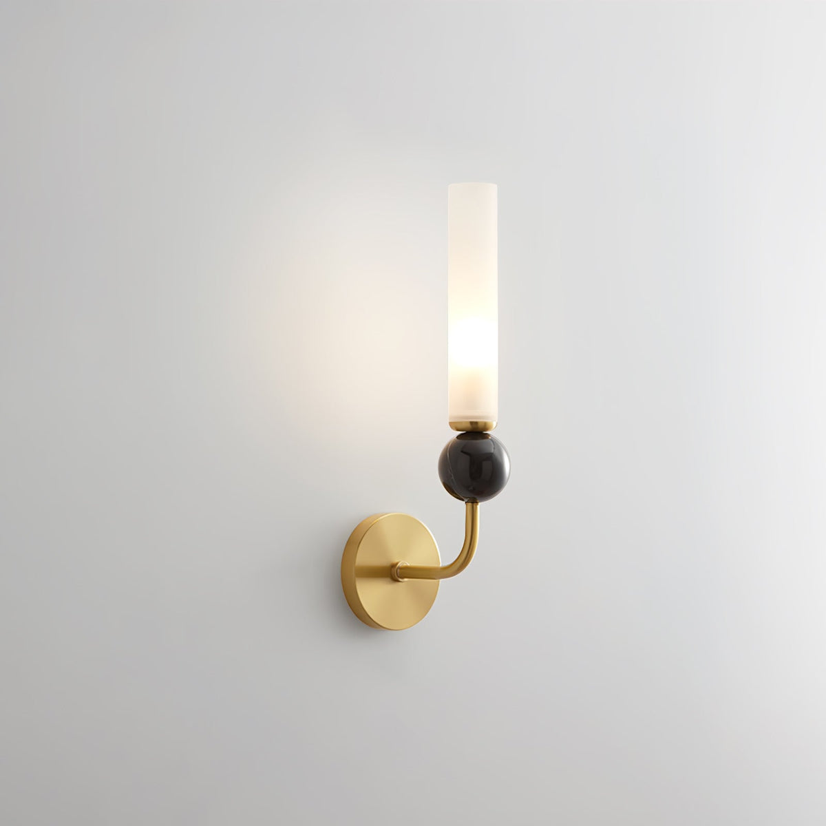 Photographed alone on white, a Clérachic brass-arm wall sconce carries a black marble orb, lit against the plain background.
