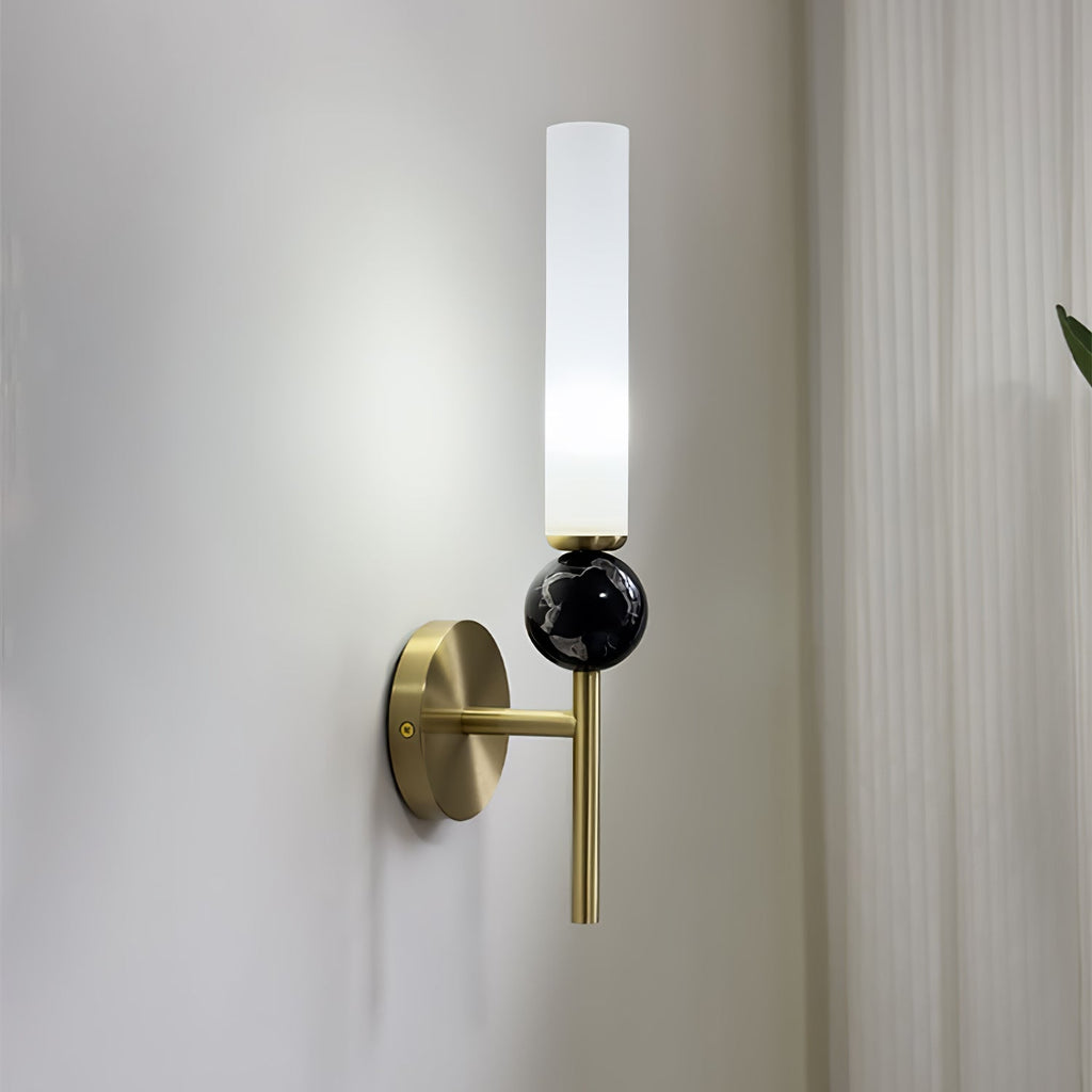Angled shot of a Clérachic brass wall sconce on a plain white wall, with a leaf visible at the edge of the frame.