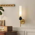 This Clérachic brass-arm wall sconce glows above a dark wood cabinet with books and a small radio, its black marble orb catching the light.
