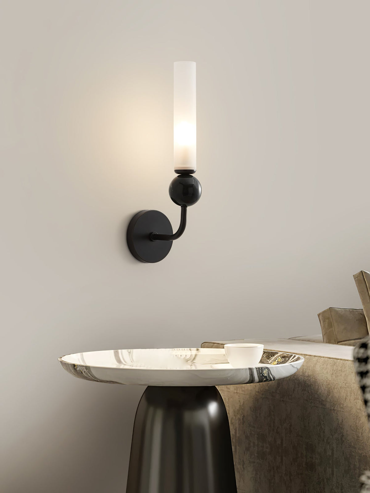 A Clérachic black wall sconce lights a curved side table holding a tray and cup in a living-room corner.