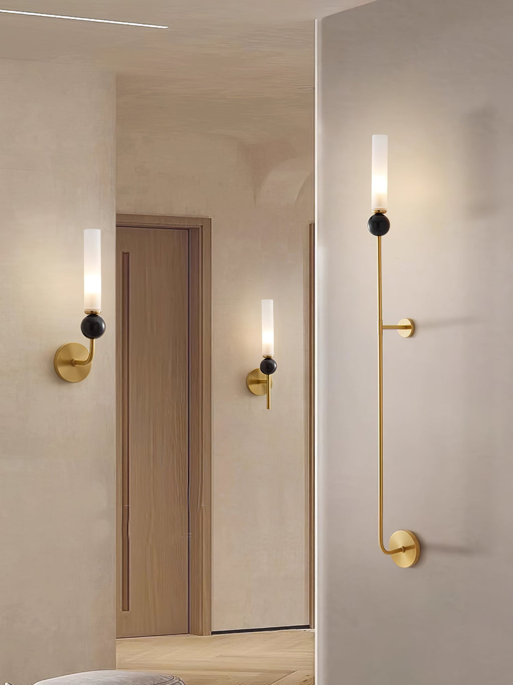 A hallway with two Clérachic brass wall sconces flanking wooden doors and a tall vertical fixture in the foreground.