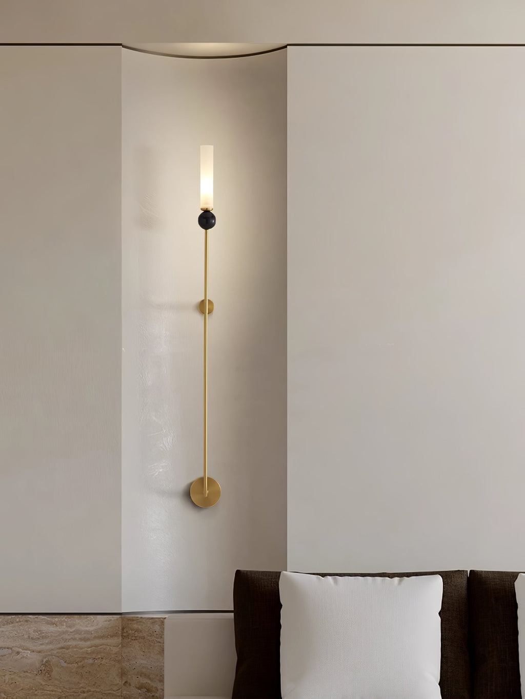 A tall Clérachic brass vertical wall light runs down a wall corner near a cushioned window nook.