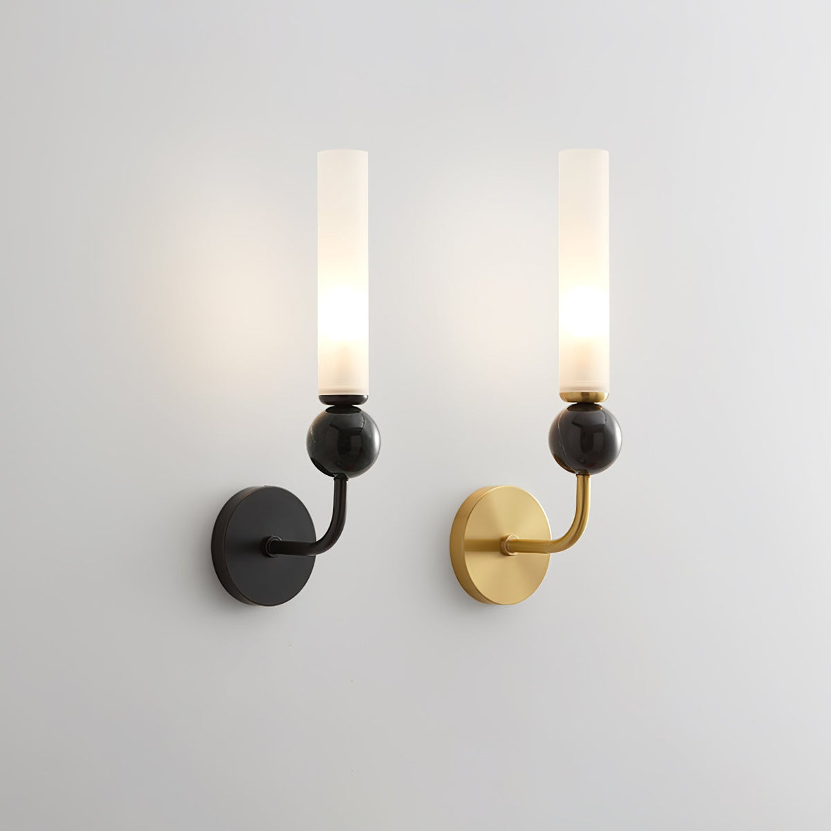 Two Clérachic wall sconces side by side on a plain grey backdrop, one in black and one in brass, both lit with black marble orbs.