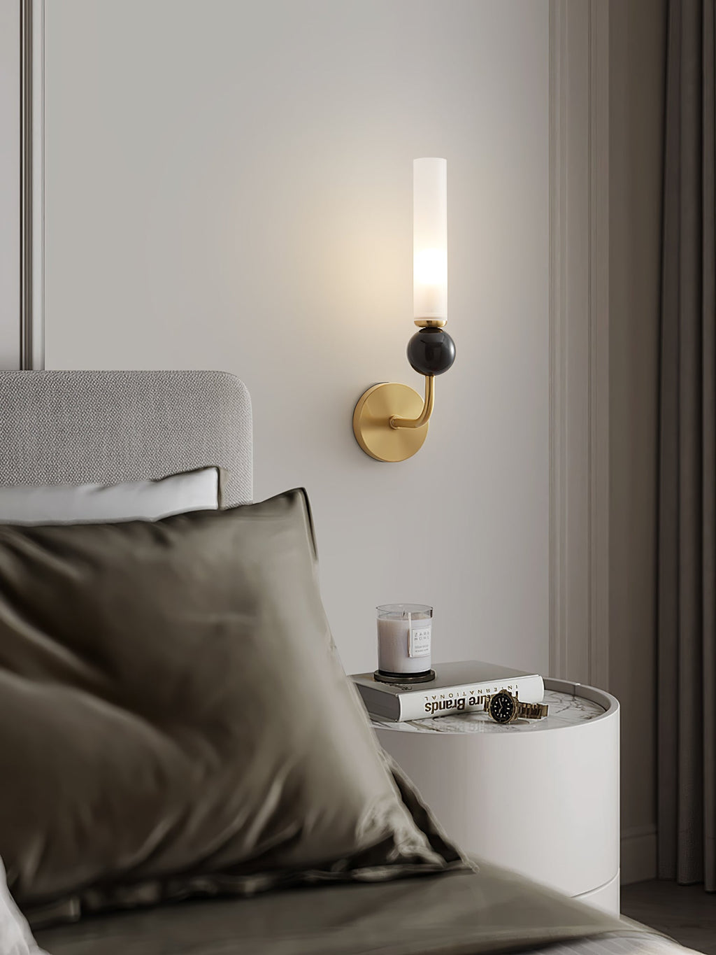 Close crop of a bedroom corner where a Clérachic wall sconce glows above a round nightstand holding a candle and books.