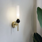 Angled shot of a Clérachic brass wall sconce with a black marble orb, a large monstera leaf visible at the edge of frame.
