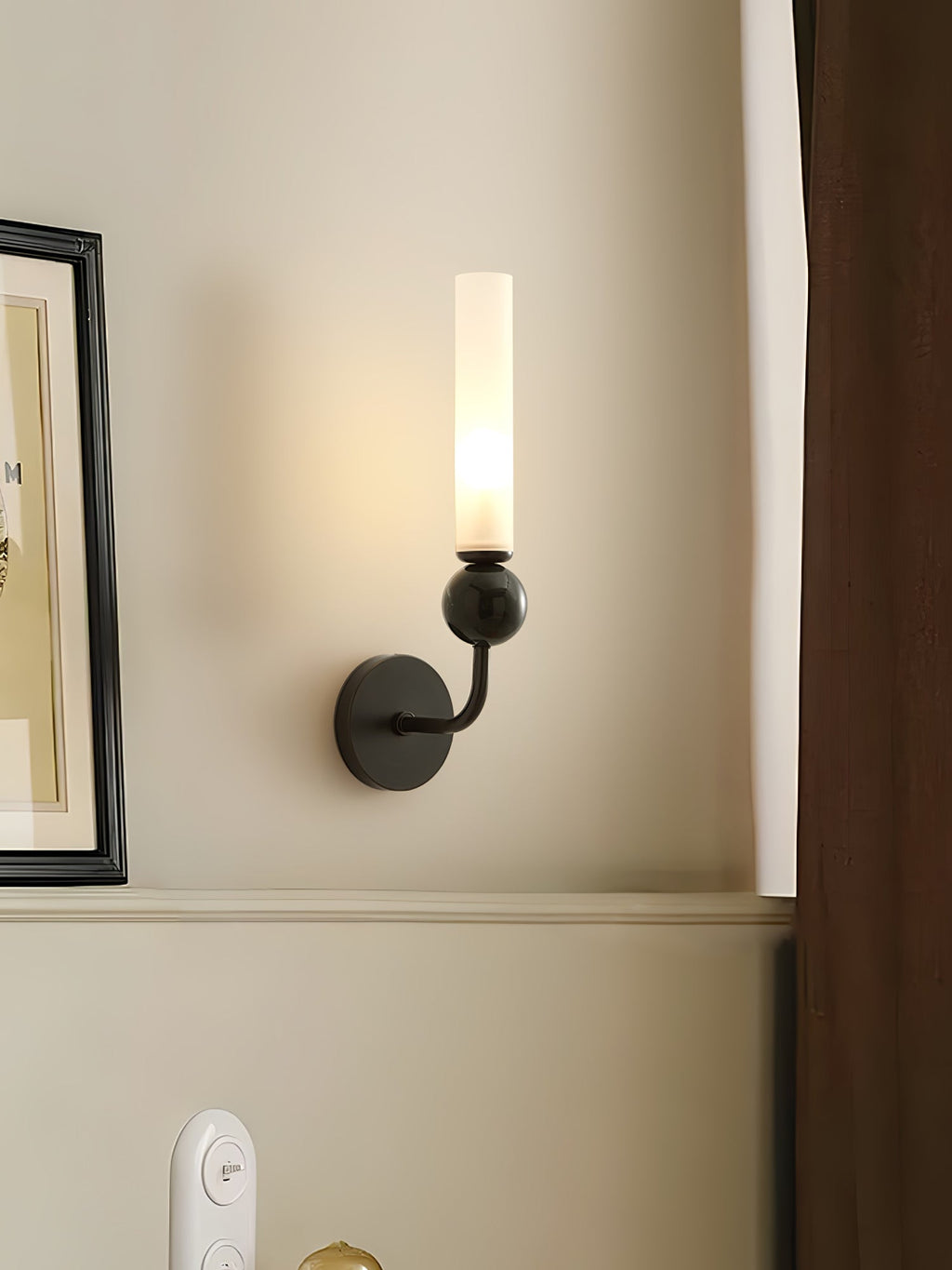 A Clérachic black wall sconce glows beside a framed picture and a wall switch plate near a dark wood door frame.